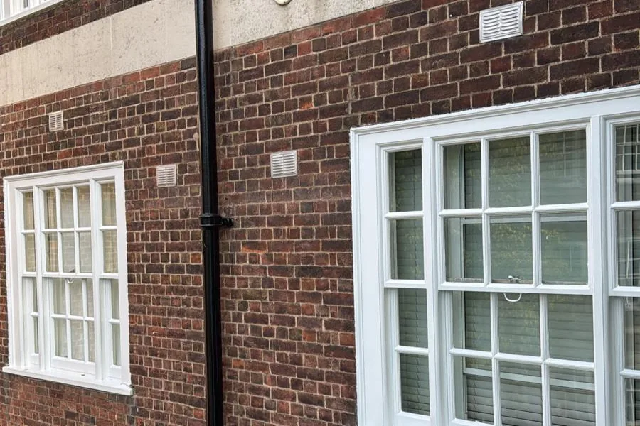 Brick facade with freshly painted white timber sash windows and cast-iron downpipe